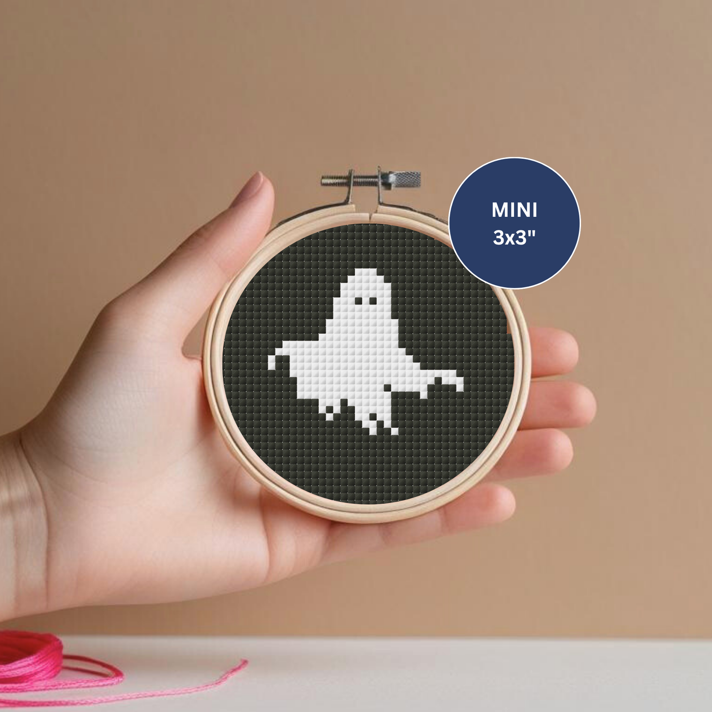 Hand holding a mini cross-stitch hoop with a ghost design on a dark background.